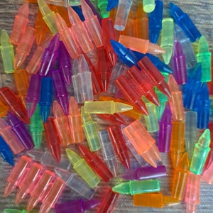 May include: A large pile of colorful plastic light-up pegs. The pegs are in various colors, including red, orange, yellow, green, blue, purple, and pink. The pegs are all pointed at one end and have a flat base.