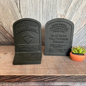 May include: Two dark gray bookends with a tombstone design. One reads "Partners in Progress" and "South Central Technical College." The other reads "South Central Technical College Mankato Campus Foundation" and "High Tech Temptations Dinner."