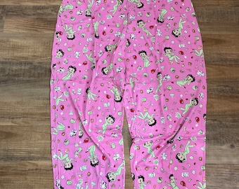 May include: Pink pajama pants with a green waistband and a repeating pattern of a cartoon woman in a green dress.