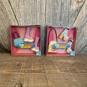 May include: Two My Scene doll accessory sets, each in a clear plastic box with a pink background. The set on the left includes a light blue purse and a pair of purple platform boots. The set on the right includes a tan purse with a floral design and a pair of blue platform boots.