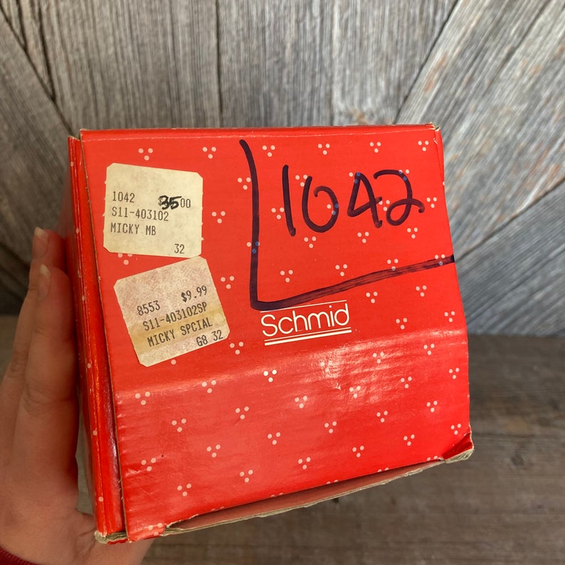 Puede incluir: Una caja de cart&oacute;n roja con lunares blancos y el texto "1042" escrito en marcador negro. La caja tiene una etiqueta blanca con el texto "1042 $11-403102 MICKY MB 32" y otra etiqueta blanca con el texto "8553 $9.99 $11-403102SP MICKY SPCIAL G8 32". La caja tambi&eacute;n tiene el texto "Schmid" escrito en marcador negro.