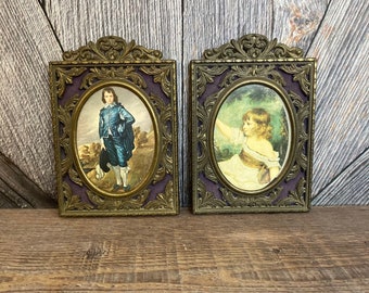 May include: Two ornate gold-toned frames with purple velvet mats, each containing a vintage portrait of a child. The portrait on the left shows a boy in a blue suit, while the portrait on the right shows a girl in a white dress.