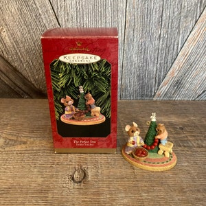 Pode incluir: Ornamento de Natal Hallmark Keepsake, The Perfect Tree, Tender Touches, com tr&ecirc;s ratinhos a decorar uma &aacute;rvore de Natal com bagas vermelhas. O ornamento est&aacute; embalado numa caixa vermelha com um r&oacute;tulo branco.