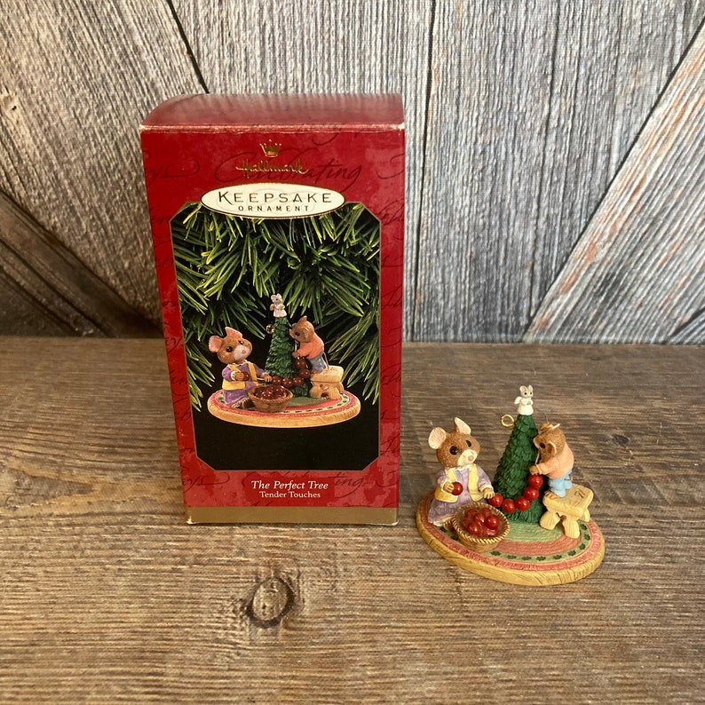 Pode incluir: Ornamento de Natal Hallmark Keepsake, The Perfect Tree, Tender Touches, com tr&ecirc;s ratinhos a decorar uma &aacute;rvore de Natal com bagas vermelhas. O ornamento est&aacute; embalado numa caixa vermelha com um r&oacute;tulo branco.