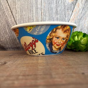 May include: Vintage Kellogg's Rice bowl with a blue background and a white rim. The bowl features a retro illustration of a smiling child and the Kellogg's Rice logo. The text "So Crispy in Milk" is also visible.