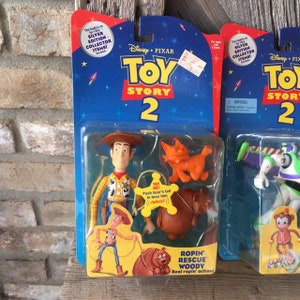 May include: Two Toy Story 2 action figure sets in their original packaging. One features Woody, a cat, and a bear. The other shows Buzz Lightyear and a monkey. The packaging is blue with the Toy Story 2 logo.
