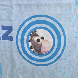 May include: Light blue fabric with a cartoon image of a horse's face inside a blue concentric circle design. The letter "N" is visible on the left side of the fabric. The horse has large eyes and a pink nose.