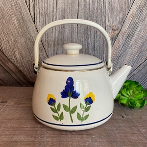 May include: White enamel teapot with a blue and yellow floral design. The teapot has a gold trim around the lid and spout.