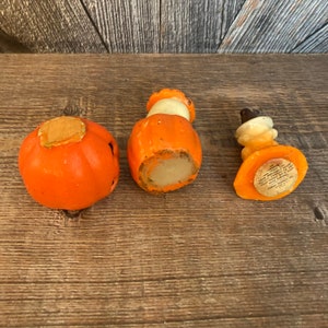 May include: Three vintage orange and white pumpkin shaped candle holders. The candle holders are made of wax and have a paper label on the bottom that reads "A.C. GILBERT CO. NEW HAVEN, CONN. U.S.A."