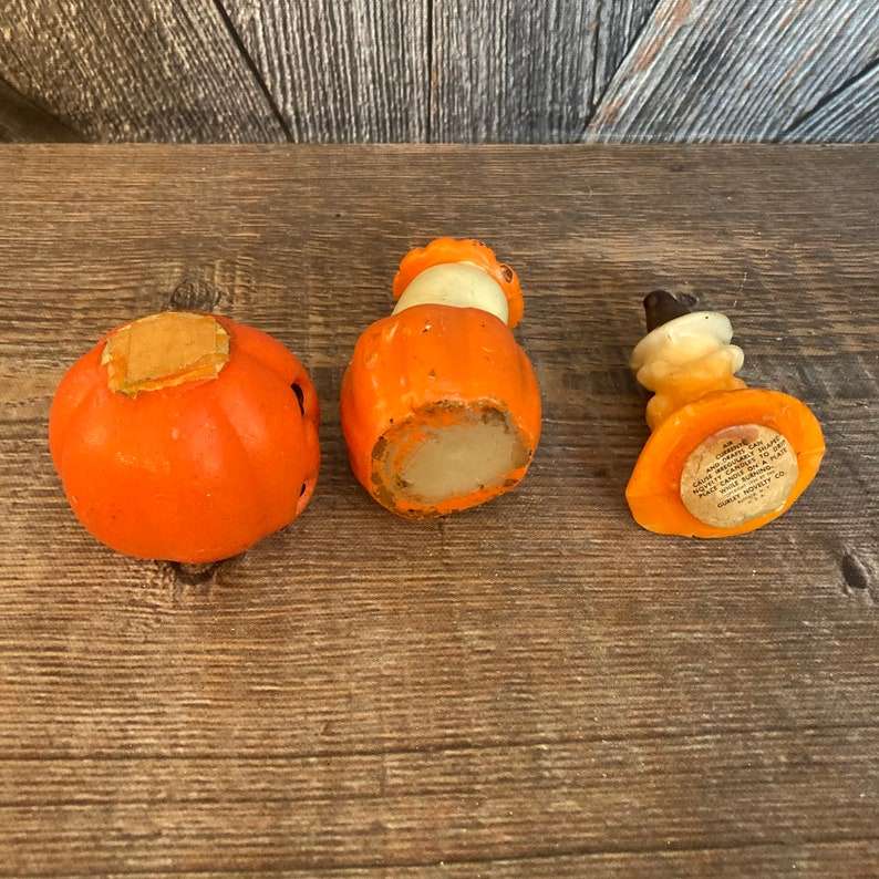 May include: Three vintage orange and white pumpkin shaped candle holders. The candle holders are made of wax and have a paper label on the bottom that reads "A.C. GILBERT CO. NEW HAVEN, CONN. U.S.A."