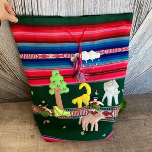 May include: A green fabric tote bag with colorful stripes and embroidered animals. The bag features a yellow llama, a white elephant, a green tree, a pink horse, and two people. The bag has a pink tassel.
