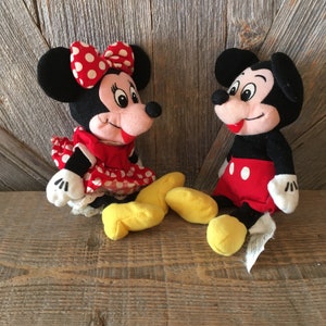 K&ouml;nnte beinhalten: Ein Paar Pl&uuml;schtiere von Mickey Mouse und Minnie Mouse. Mickey tr&auml;gt eine rote Hose mit wei&szlig;en Punkten und schwarze Schuhe. Minnie tr&auml;gt ein rotes Kleid mit wei&szlig;en Punkten, eine rote Schleife und gelbe Schuhe.