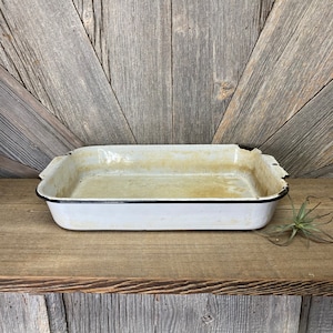 May include: White enamel baking dish with a black rim. The dish has a worn, vintage look.
