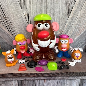 May include: A collection of Mr. Potato Head toys and accessories. The main figure is brown with a green hat and pink ears. Additional figures and accessories include hats, glasses, and a mustache.