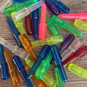 May include: A close-up of a pile of colorful plastic peg pieces for a light-up drawing board. The pegs are in various colors, including blue, green, red, orange, purple, and clear.