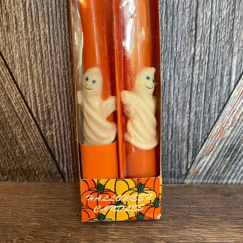 May include: A package of orange Halloween candles with white ghost figures. The candles are in a clear plastic sleeve, and the box has a pumpkin design with the words "Halloween Candles".
