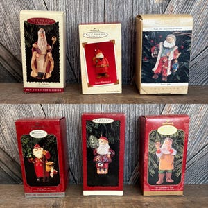 May include: Six Hallmark Christmas ornaments in their original boxes. The boxes are red and tan, featuring images of Santa Claus. The ornaments are from the New Collector's Series, Showcase, and Folk Art Americana Collection.