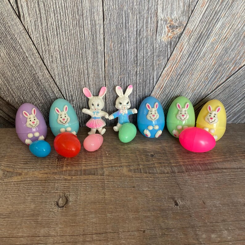 May include: Eight plastic Easter eggs, some with bunny faces, in various colors, including purple, blue, green, yellow, and pink. Two bunny figurines are also included, one in pink and one in blue.