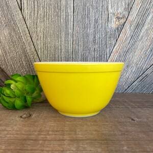 May include: A bright yellow mixing bowl with a white rim. The bowl is made of ceramic and has a smooth, glossy finish.