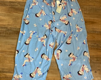 May include: Blue pajama pants with a pattern of Betty Boop characters and white flowers. The pants have a pocket on the right side.