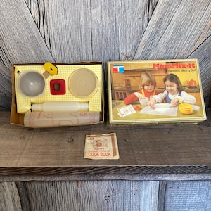 May include: Vintage Mini-Mix-It Children's Mixing Set in a yellow and brown box with a white rolling pin, two bowls, a red cookie cutter, and a yellow measuring cup. The box includes a Mini-Mix-It Children's Mixing Set Cookbook.