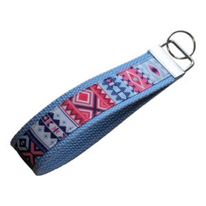 Op de afbeelding: Een blauwe sleutelhanger met een geometrisch patroon in roze, blauw en wit.