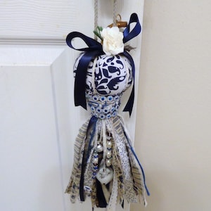 May include: A white and blue fabric pumpkin with a blue ribbon and a white flower. The pumpkin is decorated with blue and white beads and a white heart charm. The pumpkin is hanging from a white door.