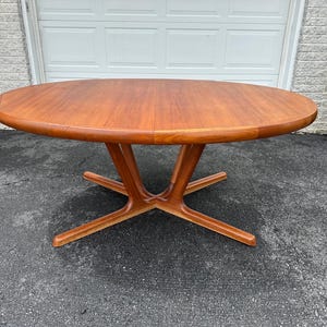 May include: A round wooden dining table with a warm, reddish-brown finish. The table has a smooth surface and a unique base with four outward-extending legs. The table is approximately 48 inches in diameter.