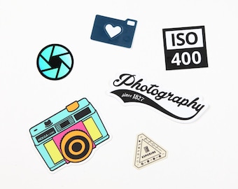 Pode incluir: Um conjunto de seis adesivos coloridos com designs temáticos de fotografia. Os adesivos incluem uma câmera, um coração, uma abertura, um rótulo de velocidade de filme ISO 400, um logotipo de fotografia e um triângulo com a palavra "exposição" dentro.