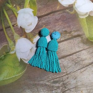 May include: A pair of turquoise tassel earrings with a beaded design. The earrings are made of small, round beads that are strung together to create a tassel shape. The tassels are approximately 7.5 cm long and are attached to a small, round bead that is about 1.25 cm in diameter.