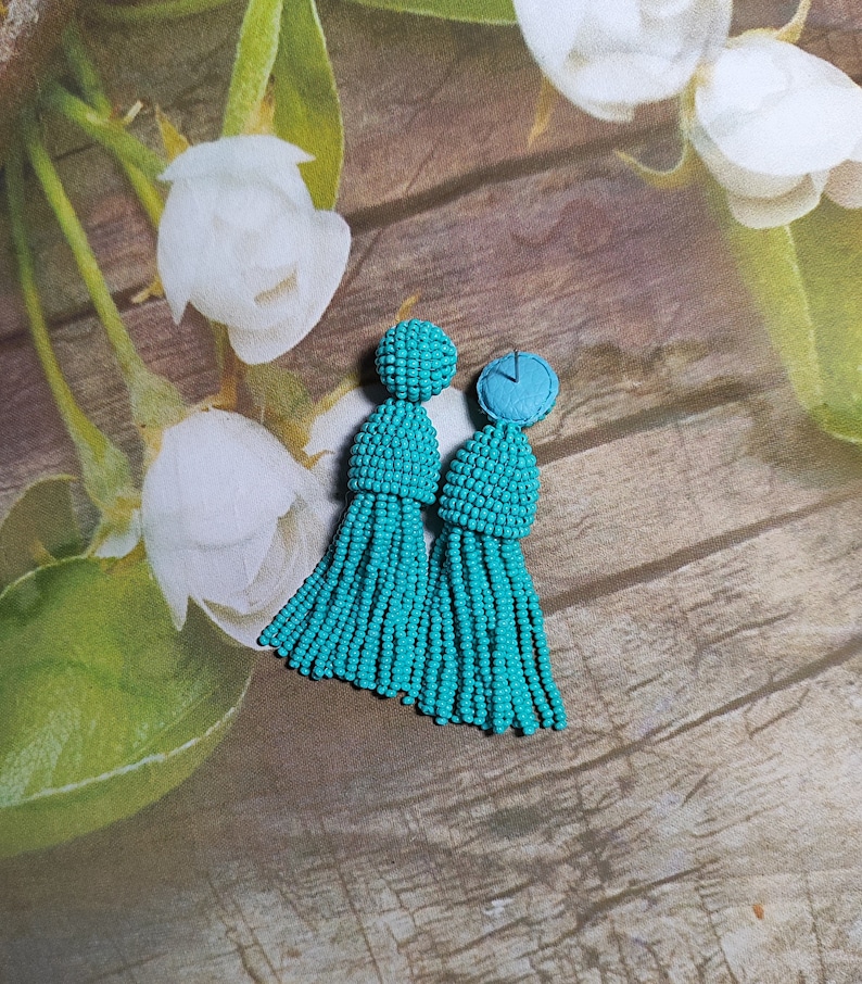 May include: A pair of turquoise tassel earrings with a beaded design. The earrings are made of small, round beads that are strung together to create a tassel shape. The tassels are approximately 7.5 cm long and are attached to a small, round bead that is about 1.25 cm in diameter.