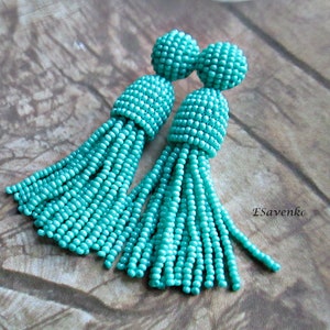 May include: A pair of turquoise beaded tassel earrings. The earrings are made of small, round beads that are strung together to create a tassel shape. The tassels are approximately 5 cm long and the earrings are approximately 7.5 cm long.