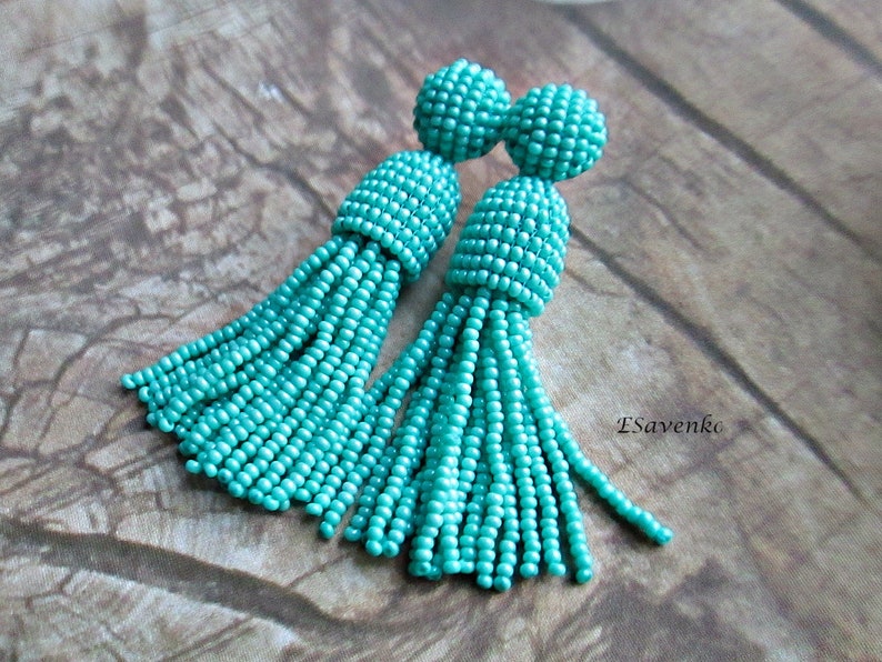 May include: A pair of turquoise beaded tassel earrings. The earrings are made of small, round beads that are strung together to create a tassel shape. The tassels are approximately 5 cm long and the earrings are approximately 7.5 cm long.