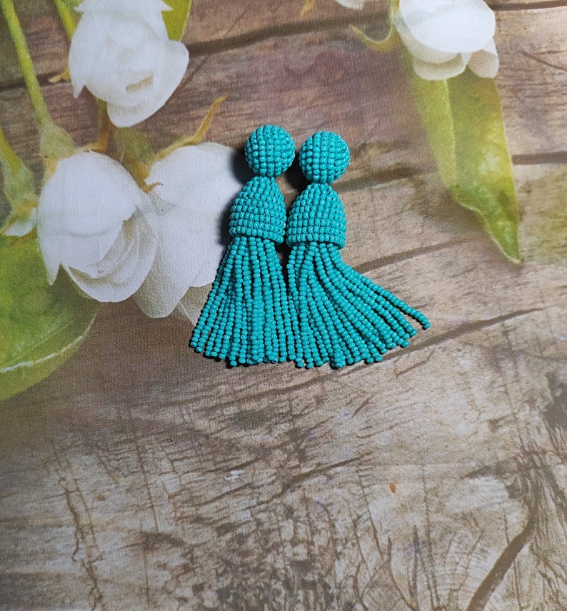May include: A pair of turquoise tassel earrings. The earrings are made of small beads and have a round top.