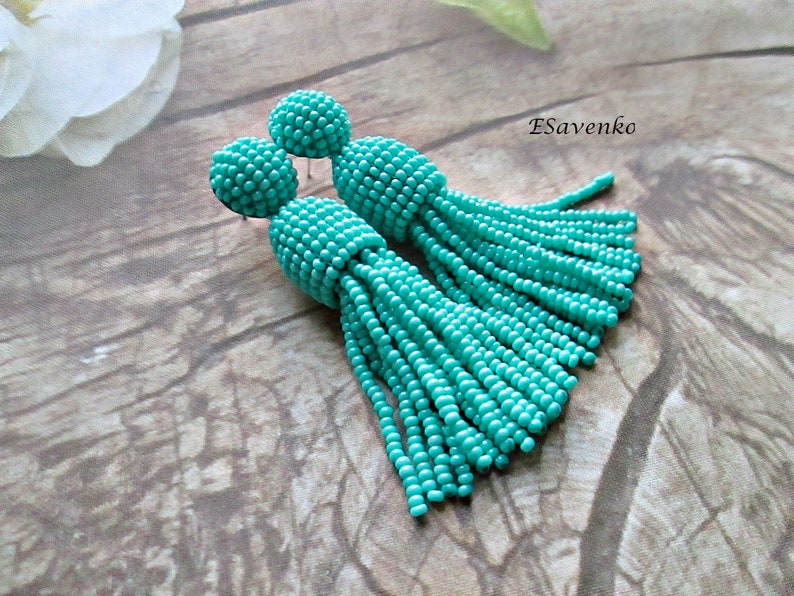 May include: A pair of turquoise beaded tassel earrings. The earrings are made of small, round beads that are strung together to create a tassel effect. The earrings are approximately 7.5 cm long.