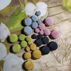 May include: Four pairs of drop earrings featuring clusters of circular, fabric-covered buttons in shades of light blue, pink, lime green, and mustard yellow, along with a pair in dark navy blue, all connected by small gold-toned metal links.