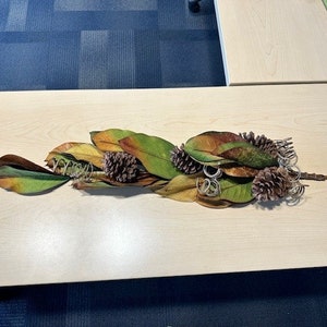 May include: A decorative arrangement of dried magnolia leaves and pinecones, with a rustic, natural aesthetic.