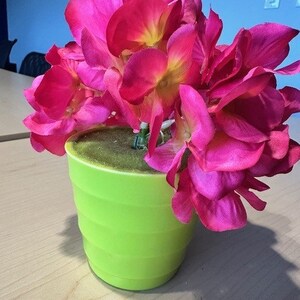 May include: A bright green planter with a cluster of pink silk flowers. The flowers are arranged in a bouquet-like shape.