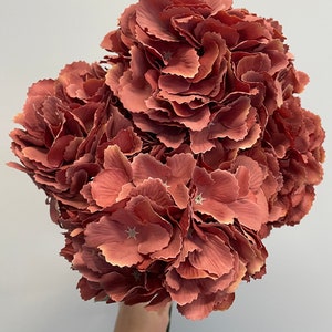 May include: A bouquet of artificial hydrangea flowers in a dusty rose color. The flowers are made of fabric and have a realistic appearance.
