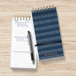 May include: A white notepad with a blue pen and a blue and white striped notepad with the text "My Daily Agenda". The white notepad has a calendar header with the date "9/6" and the days of the week "M T W T". The notepad has a list of tasks for the day, including "Recycling to the curb", "Return books to library", "Bundle clothes for donation", "Reschedule doctor's appointment", "Cardio at the gym", "Grocery store - soup on sale", and "Dues for SURD are due this week".
