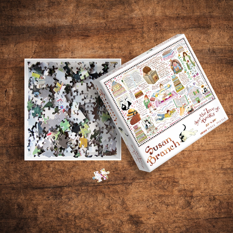 May include: A 1000 piece jigsaw puzzle featuring a colorful illustration of a cat reading a book, surrounded by books and other literary objects. The puzzle box is white with a red and black border and the text "Susan Branch For the Love of Books 27"x20" 1000 Piece Puzzle".