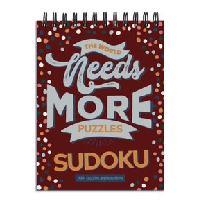 May include: A red spiral bound notebook with a colourful polka dot pattern. The cover features the text "The World Needs More Puzzles Sudoku" with a banner that reads "Puzzles" and the number "200+ puzzles and solutions".