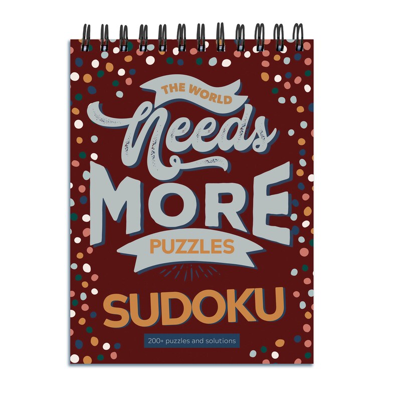 May include: A red spiral bound notebook with a colourful polka dot pattern. The cover features the text "The World Needs More Puzzles Sudoku" with a banner that reads "Puzzles" and the number "200+ puzzles and solutions".