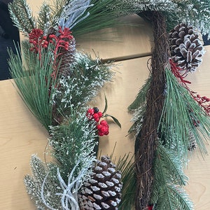 May include: A snowy artificial Christmas garland with pine needles, red berries, and pine cones.