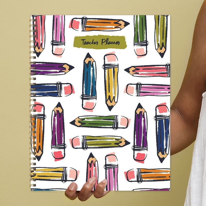 May include: A white spiral bound teacher planner with a colorful pencil pattern and the text "Teacher Planner" on the cover.