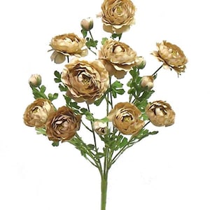 May include: A bouquet of artificial flowers featuring multiple blooms in shades of tan and brown. The flowers have a layered petal design and are surrounded by green leaves and stems. The bouquet is set against a white background.