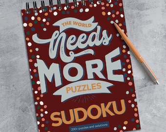 May include: A red spiral bound notebook with a colorful polka dot pattern. The cover features the text "The World Needs More Puzzles Sudoku" with the word "Sudoku" in orange. The text "200+ puzzles and solutions" is printed at the bottom of the cover.