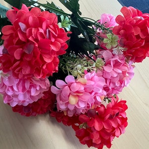 May include: A bouquet of pink and red artificial flowers. The flowers are arranged in a cluster and have a realistic appearance.