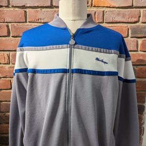 May include: A gray, blue, and white striped zip-up jacket with the text "MacGregor" embroidered on the right side of the chest.