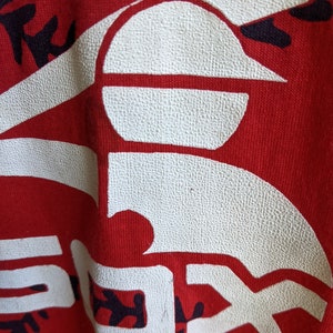 May include: Close-up of a red fabric with a large white "SOX" logo, a baseball, and baseball stitching. The logo has a textured appearance. The background is a solid red color. The image is of a sports-themed item.